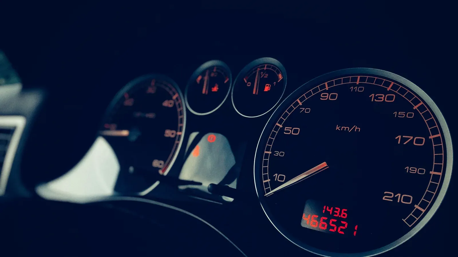 A car speedometer and dashboard gauges lit at night