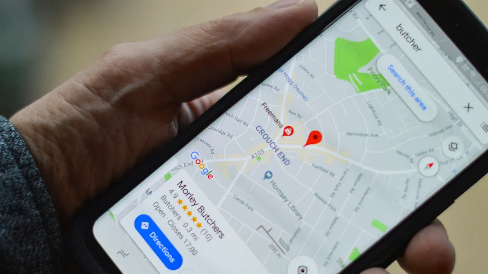 A hand holding a phone that shows a local butcher's listing in Google Maps