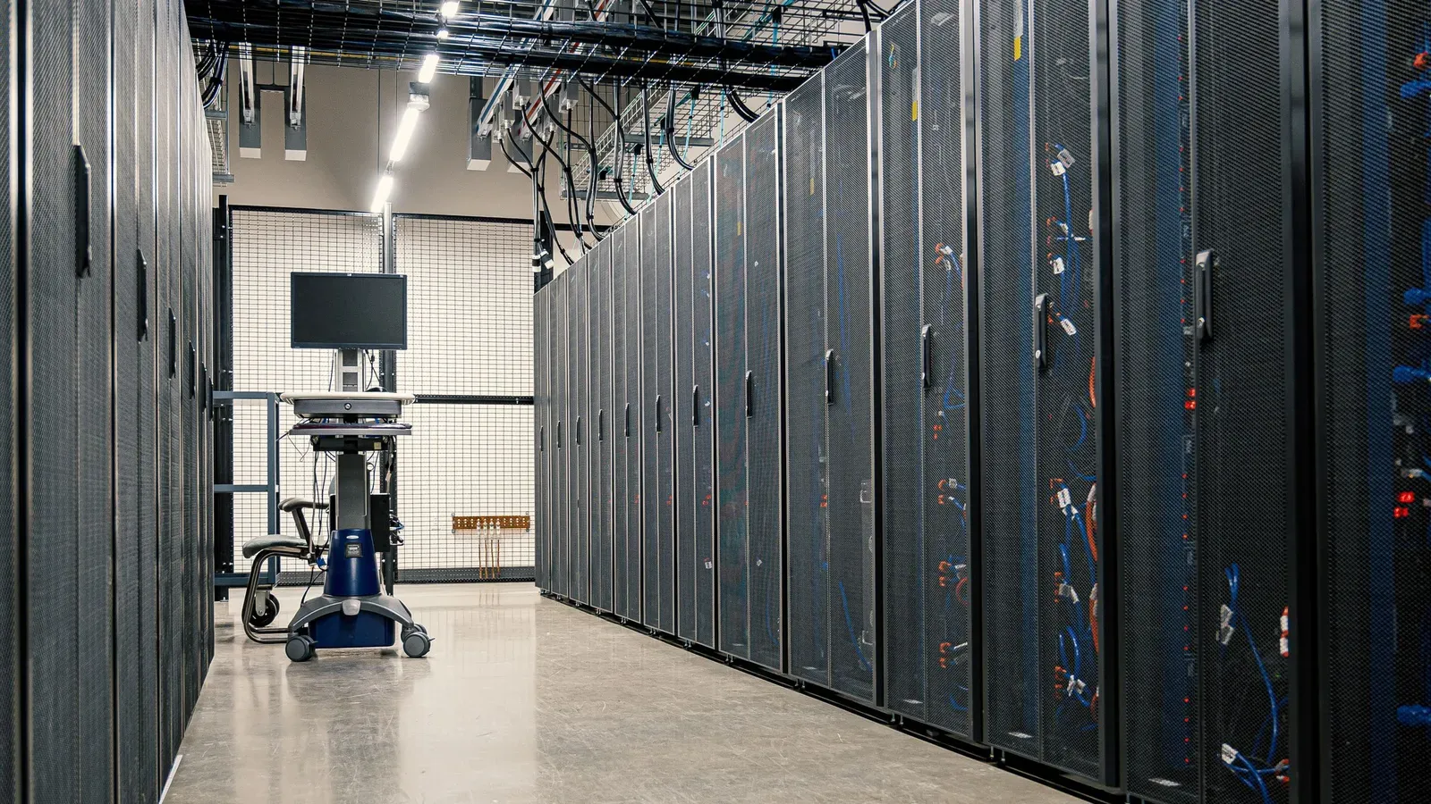 A corridor between rows of server racks in a data centre, with cables and equipment visible in the cabinets
