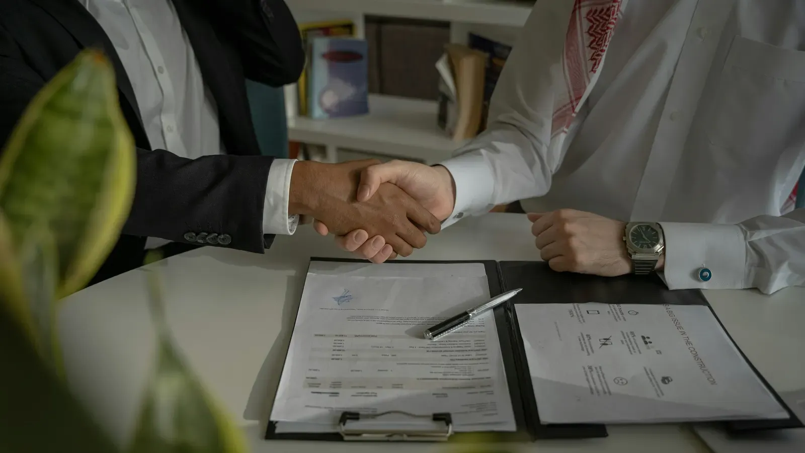 Two people shaking hands over a signed paper agreement