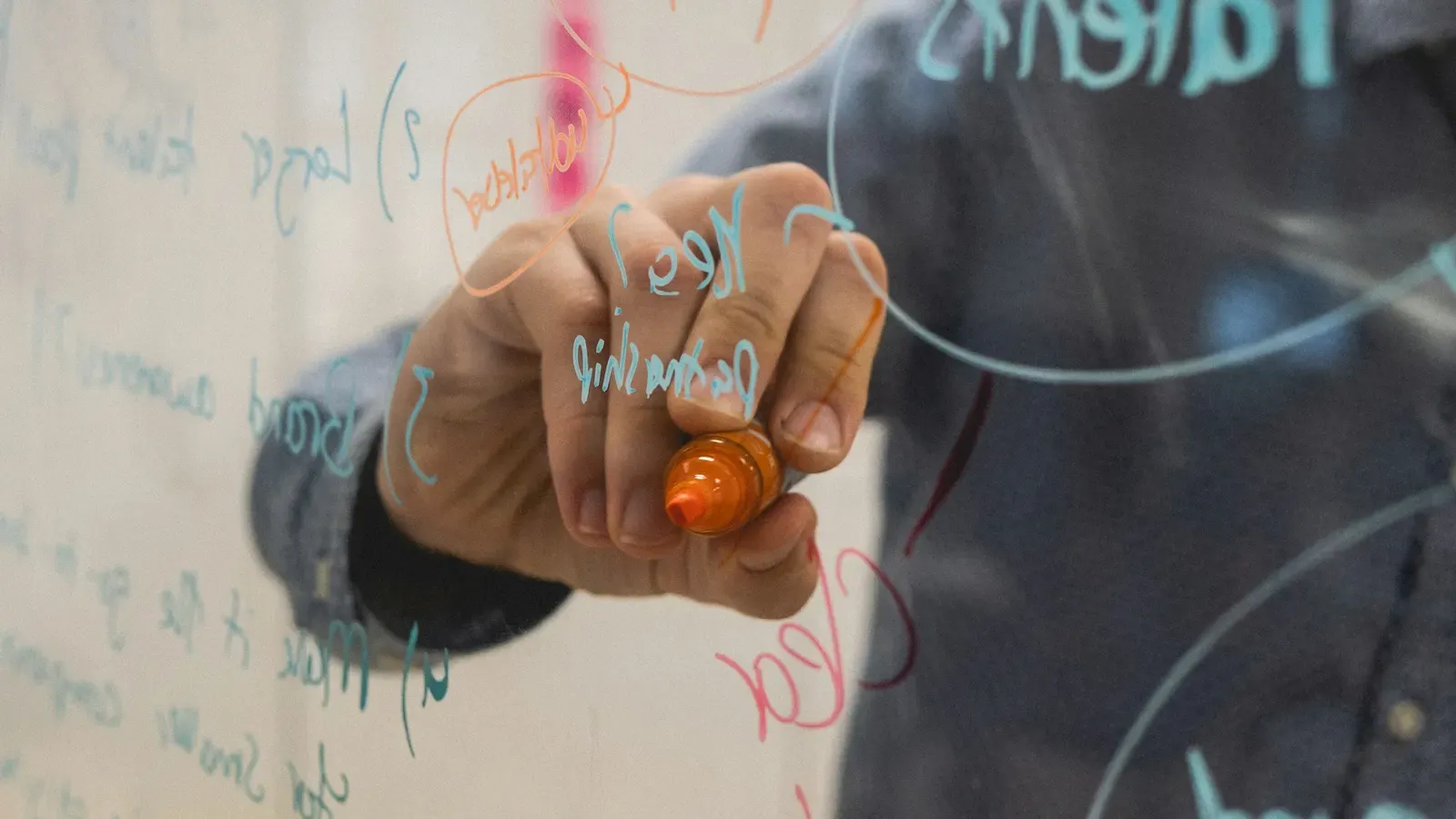 A person drawing a product plan and diagrams on a glass whiteboard